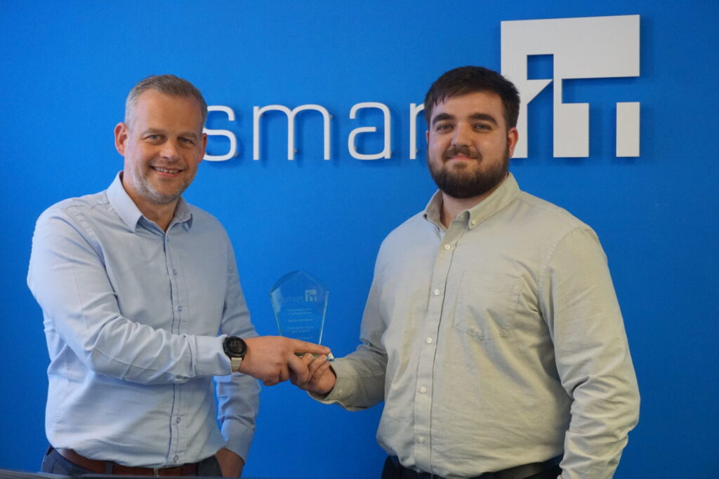 Two men shaking hands in front of Smart IT logo at celebration event.