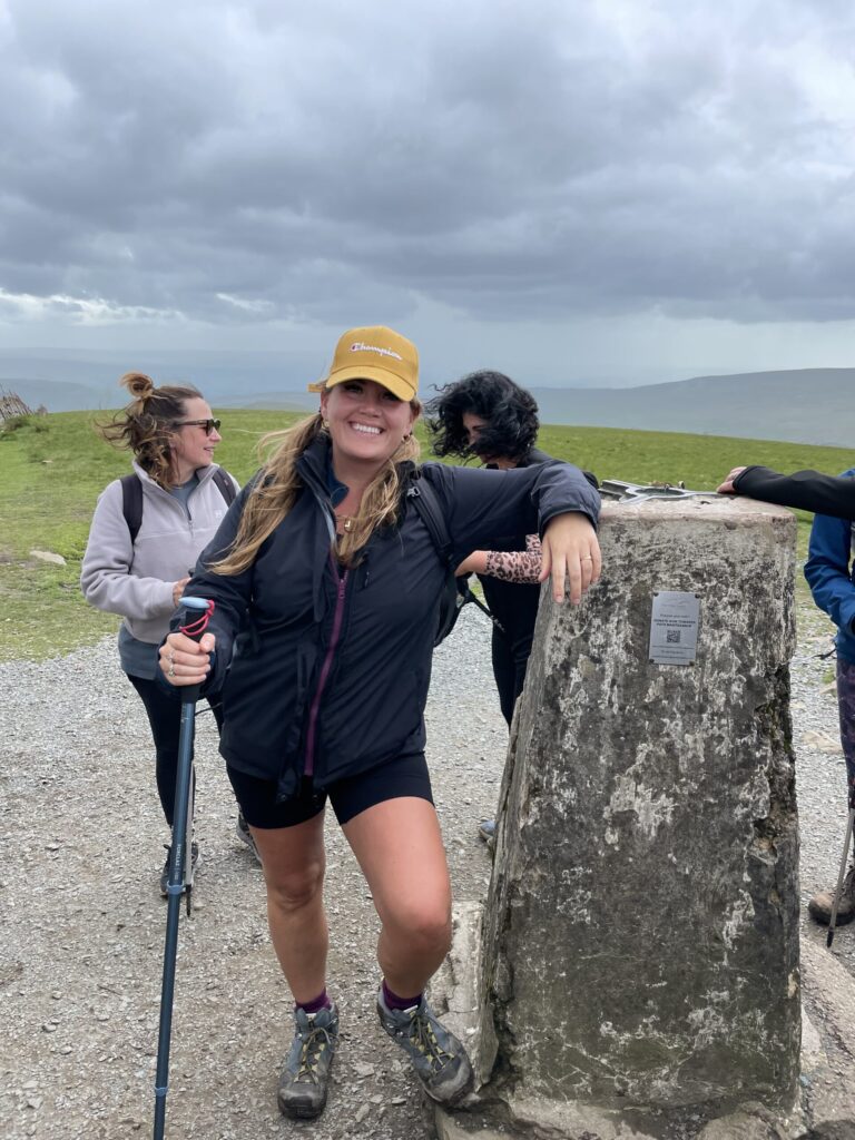Woman smiling at summit marker during Yorkshire Three Peaks challenge.