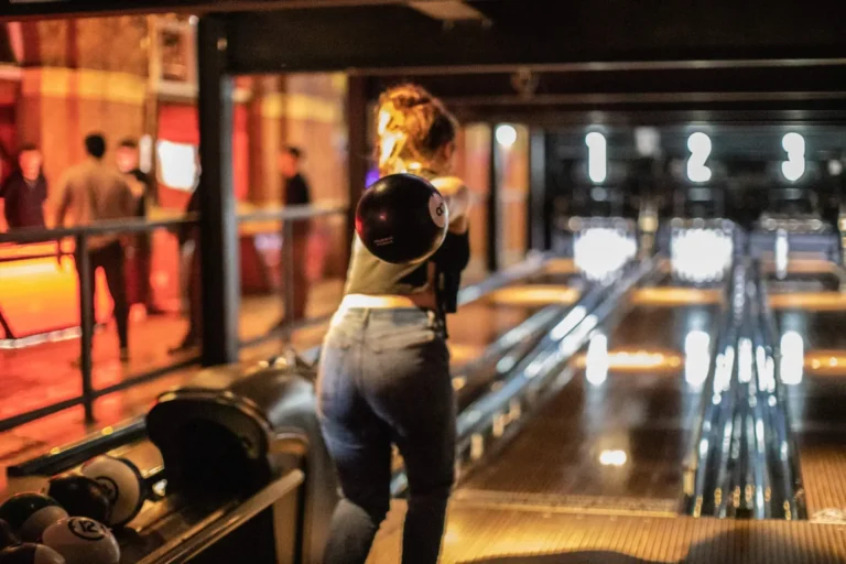 Woman bowling at night with friends in a lively bowling alley.
